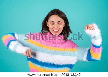 Young woman in a bright multicolored sweater on a blue background, smiles, moves cheerfully, dances alone