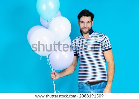 Celebration Ideas. Positive Tranquil Caucasian Handsome Brunet Man With Bunch of Colorful Air Balloons Posing Against Blue Background. Horizontal Image