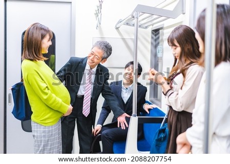 A man gives up his priority seat to a pregnant woman. Royalty-Free Stock Photo #2088207754