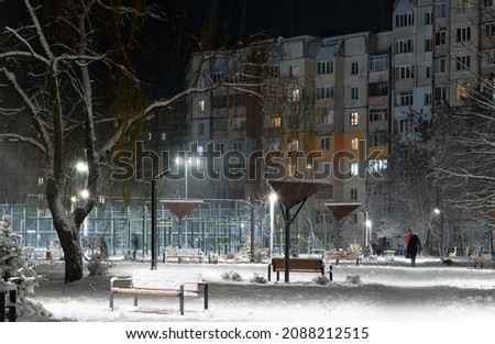 Evening landscape of residential area with snow-covered alley and bright lighting