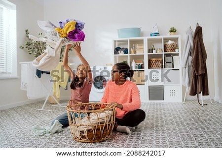 Girl is sitting on floor in bathroom with mother and disturbs while she is sorting clothes for washing daughter is bored and for fun throws clothes up in background washing machine dryer liquids