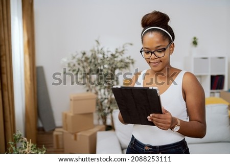 Smiling attractive girl orders furniture for new apartment online, decorating home after moving, looking for decorating inspiration, using tablet
