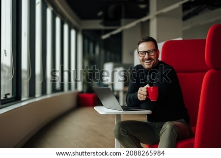 Picture of joyful adult man, ending his shift in the office with a cup of tea.
