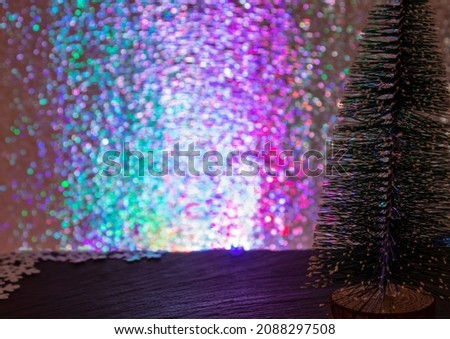 Colored background with free space for text or logo.
New Year's atmosphere. Selective focus and blurry multi-colored bokeh. Small decorative Christmas tree in the foreground.