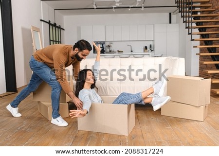 Happy multiracial couple first time home buyers having fun while unpacking belongings on moving day. Excited wife riding in cardboard box while her husband push it in new house apartment Royalty-Free Stock Photo #2088317224