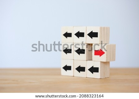 Wooden block with red arrow opposite black arrow to show concept individual and standing out from the crowd isolated on table background.