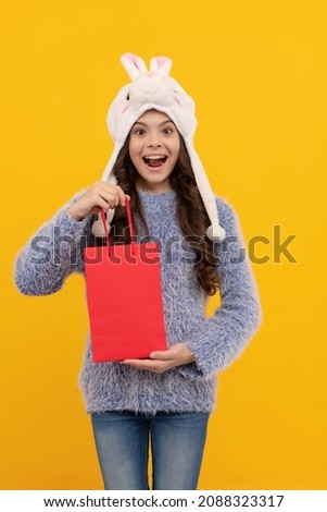 happy kid long hair in hat hold pack on yellow background, new year