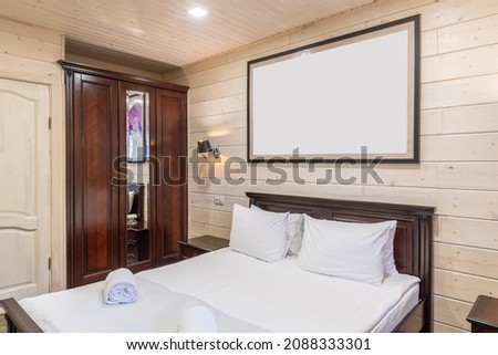 interior of a bedroom with a large double bed and a picture above the headboard, finishing the room with natural cream wood, a mahogany wardrobe with a mirror