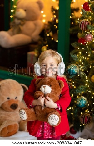new year girl in fur headphones beautiful cute funny gifts joy happiness red dress coat blonde child cute smile sweet bear bears glass ball kukry shop kids christmas lights green interior insulation 