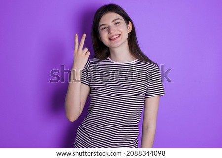 Caucasian woman wearing striped T-shirt isolated over studio background smiling and looking friendly, showing number two or second with hand forward, counting down