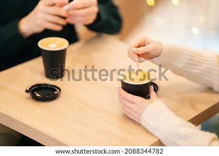 Close-up top view of woman and man sitting in cafe holding warm cups of coffee on table having fun conversation. Young couple enjoying time spending with each other sitting at table in coffee shop Royalty-Free Stock Photo #2088344782