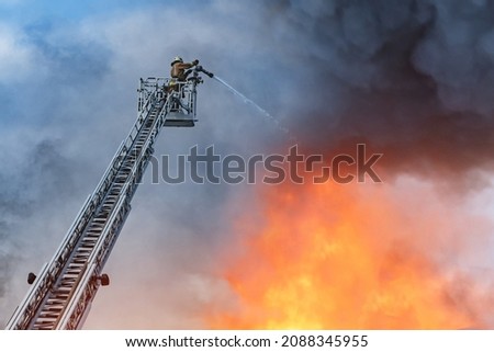 Fire extinguishing. Firefighter on the stairs extinguish a big fire. A firefighter with a water hose on the stairs. A firefighter on the background of fire and smoke. Fireman extinguishes a large fire