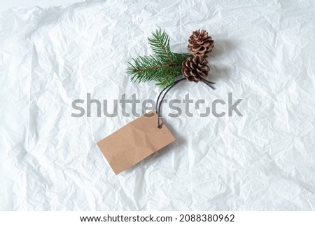 Close up of green fir branch and pine cones with blank white label. Price tag mockup scene on tissue paper background. Christmas composition, top view, flat lay