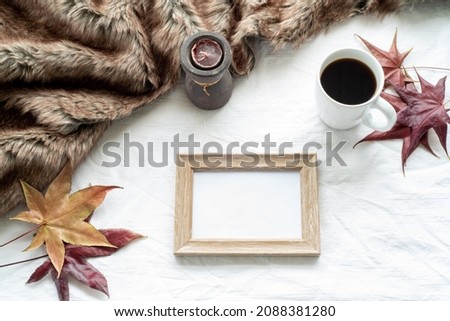 Autumn breakfast scene. Blank wooden picture frame mock-up with maple leaves, cup of coffee, scented candle and plaid. White tablecloth background. Top view, flat lay