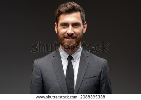 Portrait of happy good looking businessman in formal suit smiling to the camera in front of black wall background. Stock photo 