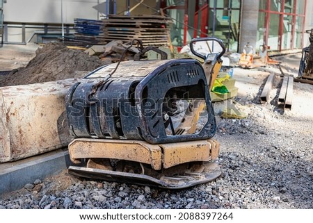 Vibratory rammer with vibrating plate on a construction site. Compaction of soil for further construction work. Close-up Royalty-Free Stock Photo #2088397264