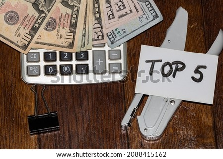 Dollars on calculator and white label with text Top 5 on it. Royalty-Free Stock Photo #2088415162