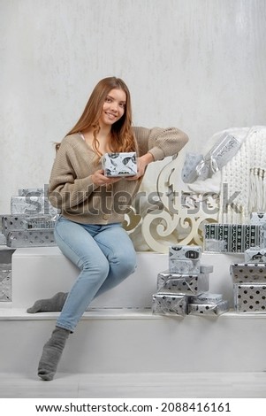 a young woman smiling is sitting in a New Year's interior with a gift in her hands