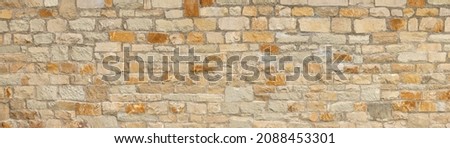 Light brown stone wall in panoramic close-up made of old, roughly hewn, different natural stones