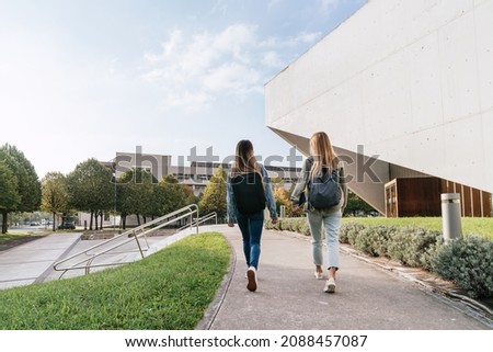 Rear view of two college classmates leaving the university together while talking. Royalty-Free Stock Photo #2088457087