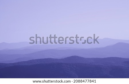 low mountains in mist toned in trendy Very Peri color pantone of the Year 2022. unspoilt hilly nature of haze away from man