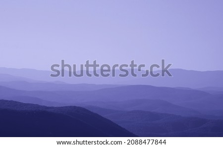 low mountains in mist toned in trendy Very Peri pantone color of the Year 2022. unspoilt hilly nature of haze away from man