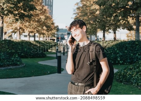 Master study concept.Happy student man receiving a call on the smart phone walking in city college campus with backpack and having good news. Copy space. Close up portrait during a sunset.