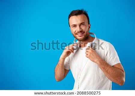 Young man in casual white t-shirt with headphones against blue background