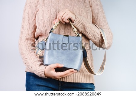 A young woman in a beige sweater holds a bag in her hands. Fashionable look for autumn