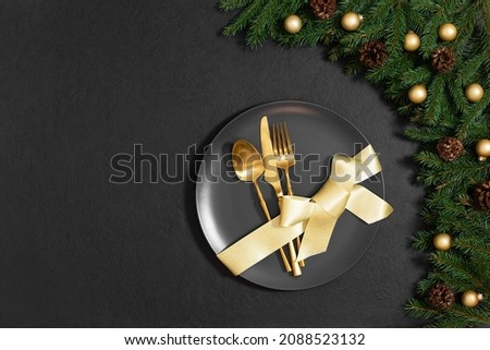 Christmas table setting with gold cutlery and bow in a plate on black background. Happy new year. Space for text. Top view, flat lay.