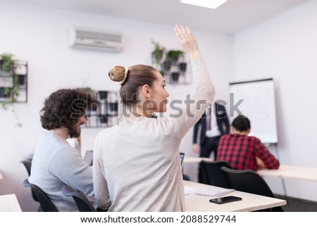 Students listening to a lecturer in a classroom. Smart young woman rasing hand during class.