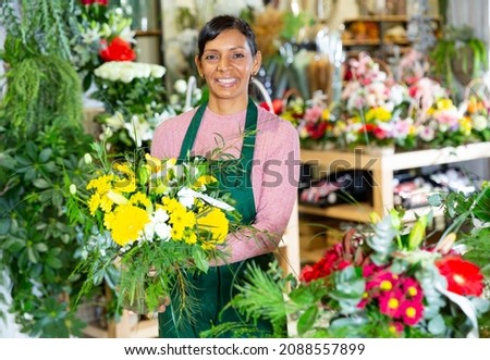 Positive mexican female florist in apron holding composition from natural flowers at flower shop Royalty-Free Stock Photo #2088557899