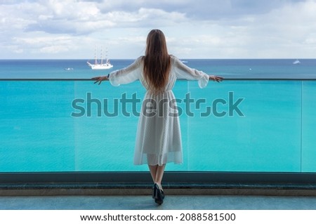 beautiful young woman from the back stands on the balcony and looks at the sea Royalty-Free Stock Photo #2088581500