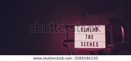 Director chair with behind the scene banner light box. Letterboard text Lightbox or Cinema Light box. Movie clapperboard and Director chair. Black Background. Represent video behind the scenes is on.