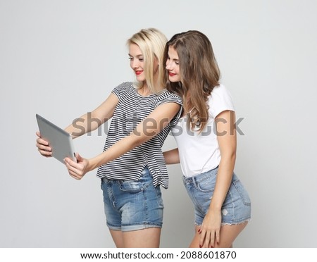 technology, friendship and people concept - two smiling young women with tablet pc over grey background.