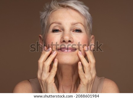 Portrait of gorgeous happy mature woman, senior older 60 year lady looking at camera touching her face Royalty-Free Stock Photo #2088601984