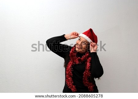 Latin adult woman with hat and Christmas garland shows her enthusiasm and happiness for the arrival of December and celebrate Christmas

