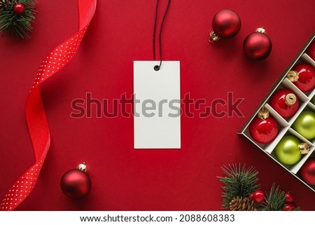 Christmas sale and holiday fashion design concept. Blank clothing tag and xmas decoration and ornaments on red paper background as flatlay mockup.