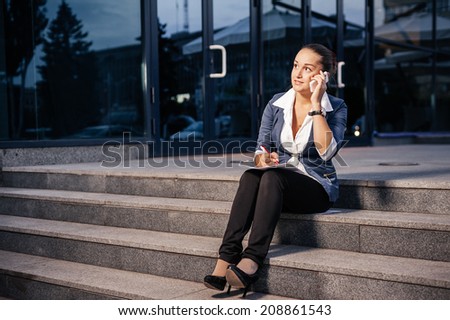 Successful businesswoman or entrepreneur taking notes and talking on cellphone while walking outdoor. City business woman working.