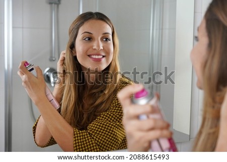 Beautiful young woman applying dry shampoo on her hair before going out. Fast and easy way to covering grey hair with instant spray dye. Royalty-Free Stock Photo #2088615493