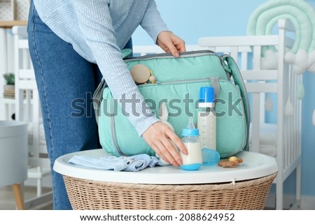Woman with bottles of milk for baby and bag in room Royalty-Free Stock Photo #2088624952