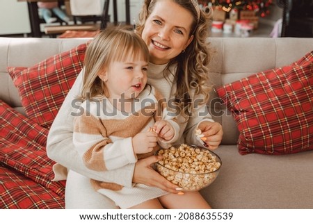 Happy young mom and baby girl laugh while sitting on the couch and eat popcorn. family watching TV and eating popcorn.