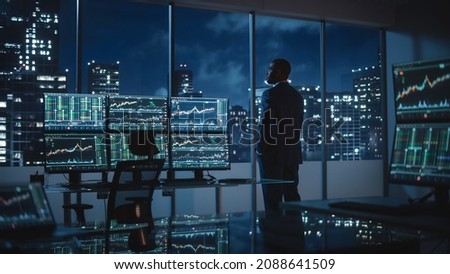 Successful Businessman Looking Out of the Window on Late Evening. Modern Hedge Fund Office with Computer with Multi-Monitor Workstation with Real-Time Stocks, Commodities and Exchange Market Charts. Royalty-Free Stock Photo #2088641509