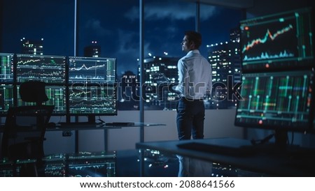 Financial Analyst Using Laptop Computer, Standing Next to Multi-Monitor Workstation with Real-Time Stocks, Commodities and Exchange Market Charts. Businessman Working in Broker Agency Office. Royalty-Free Stock Photo #2088641566