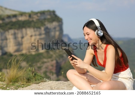Happy asian woman wearing headphones listening to music in a cliff