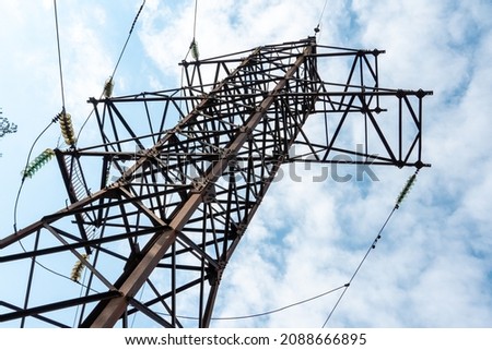 View of the tower of a high-voltage power line against the background of blue sky and clouds. Voltage power lines