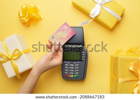 Female hand with credit card, payment terminal and gifts on color background