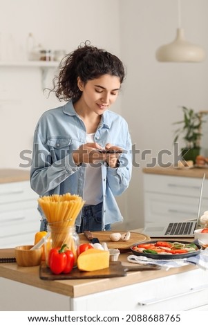 Young woman taking photo of fresh mushrooms in kitchen