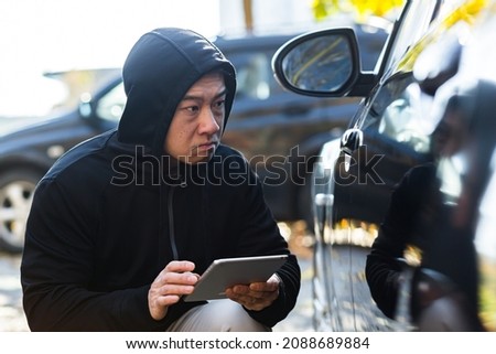 male bandit thief car thief asian uses a tablet to turn off the car alarm