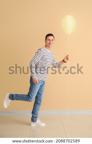 Young man with balloon against color background